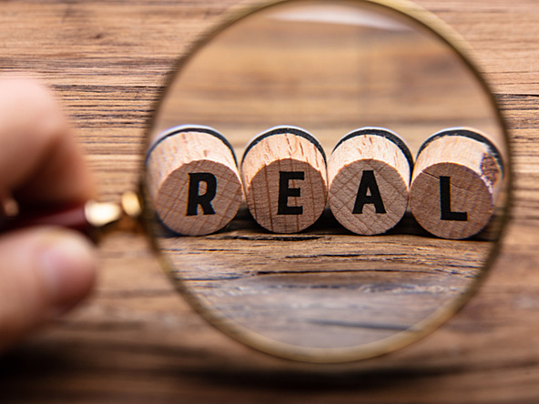 magnifying glass looking at word REAL spelled on wooden blocks